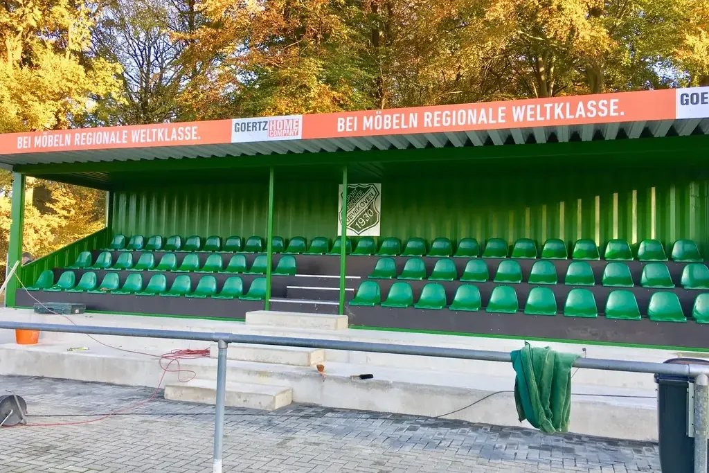 Die fertige Container-Tribüne mit grünen Sitzen am Kunstrasen